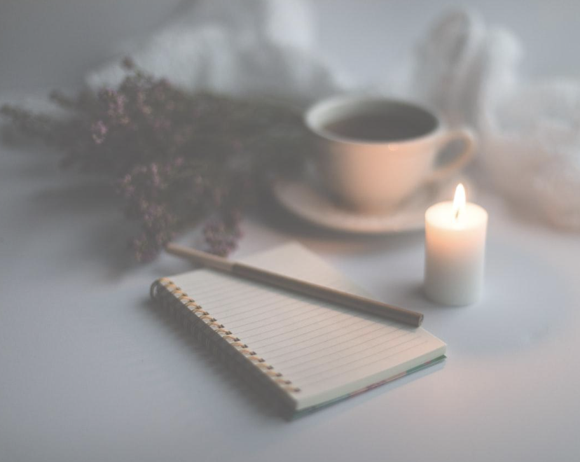 A calm morning scene with a journal, candle, and cup of tea on a table